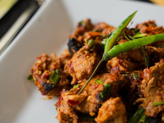 A Plate Of Spiced Meat Garnished With Sliced Green Chilies On A White Square Plate. A Fork Is Beside The Plate.